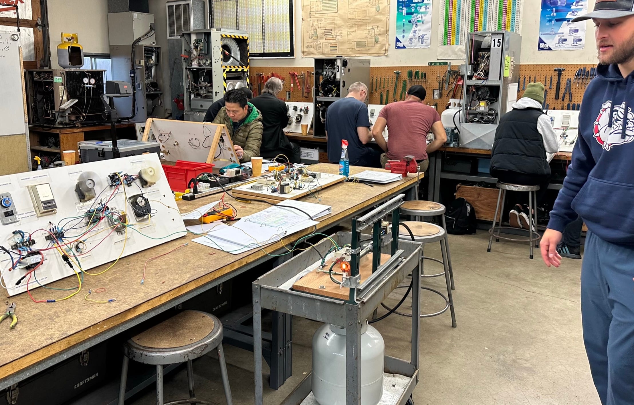 Students working at electrical trainers and open HVAC units across the training lab